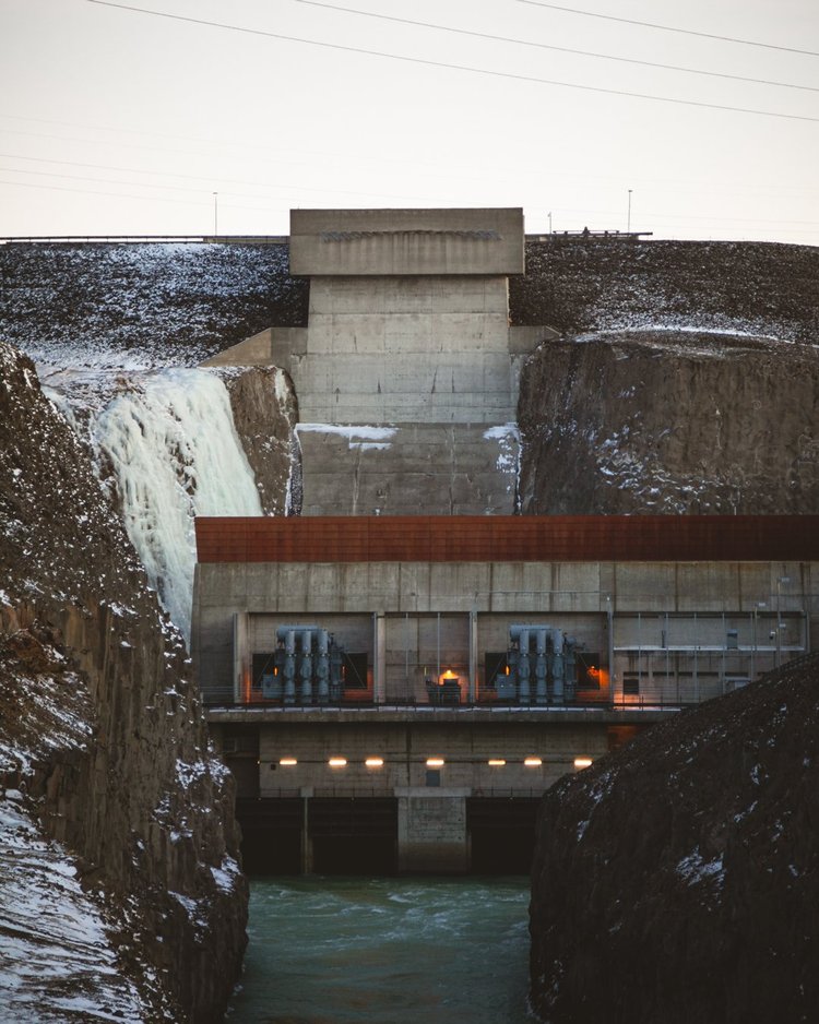 Ein Wasserkraftwerk mit überlaufendem Stausee und Schnee in der felsigen Umgebung.