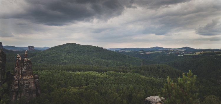 Bewaldete Hügel unter einem wolkigen Himmel, mit Felsformationen im Vordergrund.