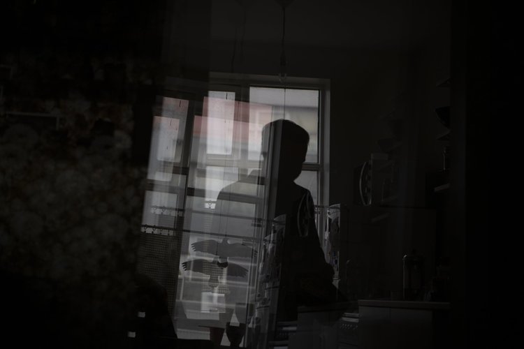 Eine Person als Silhouette in einem dunklen Innenraum am Fenster, mit Spiegelungen von Gebäuden und einem Adlerbild.
