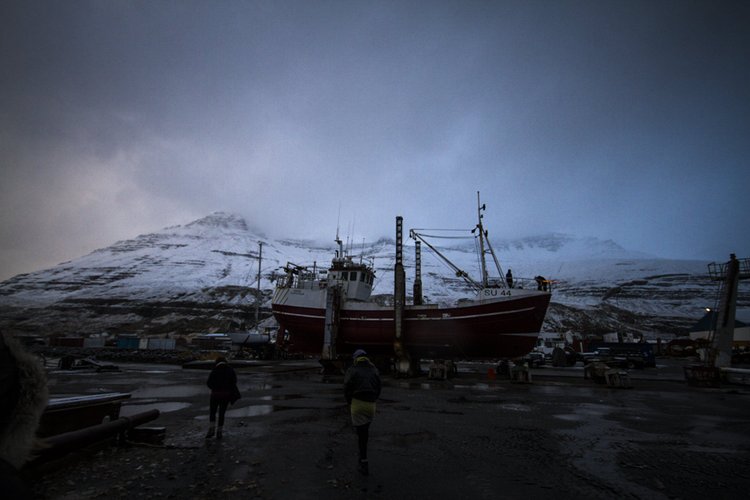 Ein Fischerboot in einer Werft, umgeben von schneebedeckten Bergen unter dunklem Himmel.