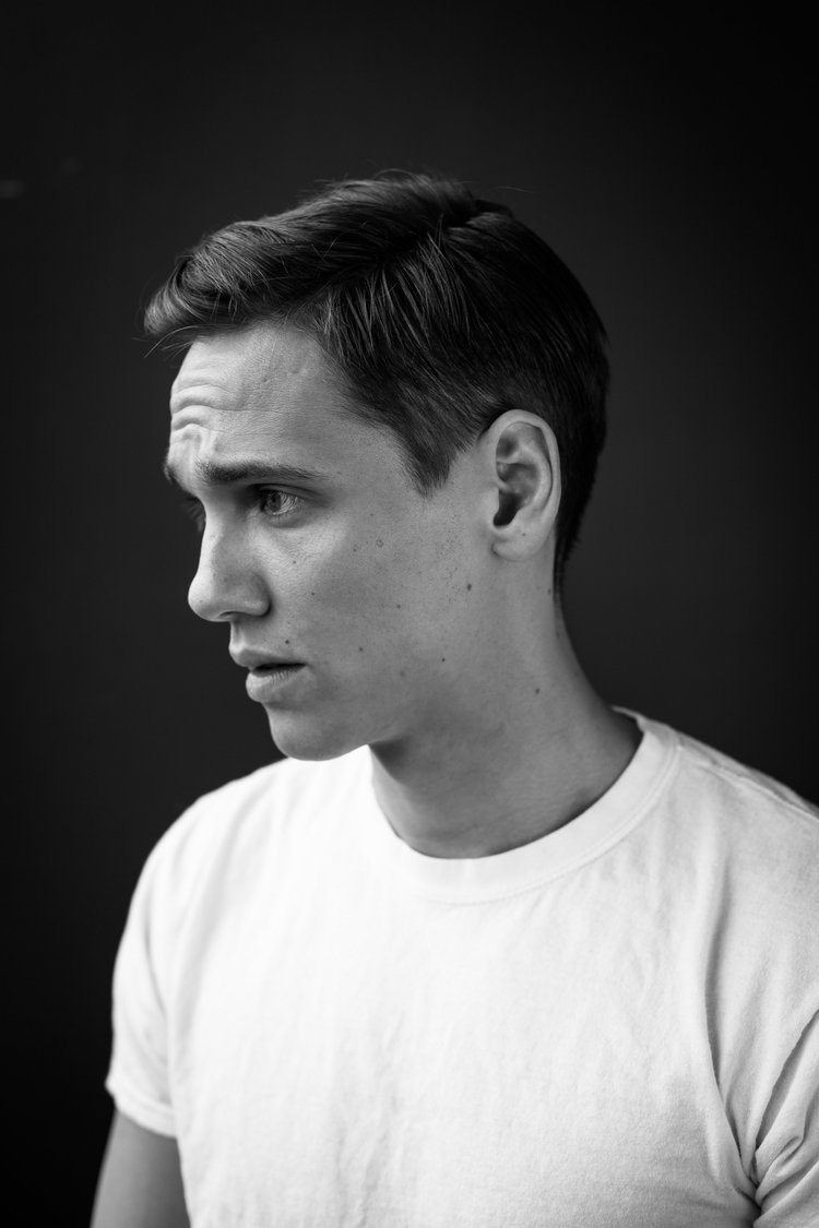Schwarzweißporträt eines jungen Mannes mit kurzen Haaren und weißem T-Shirt im Profil.