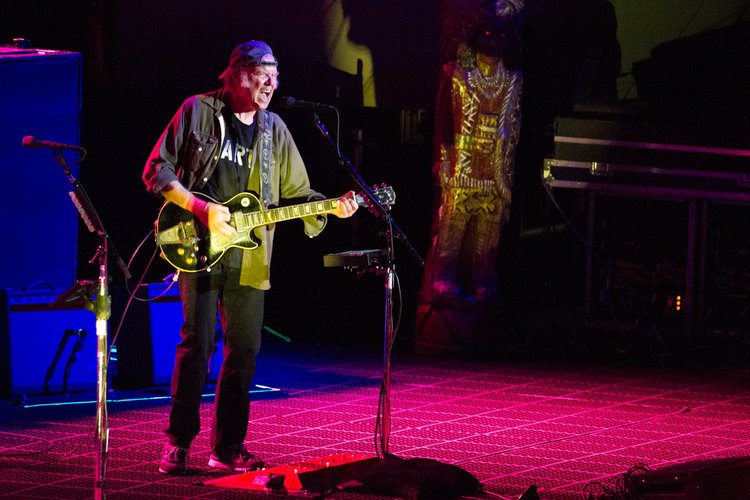 Ein älterer Mann mit umgedrehter Kappe spielt E-Gitarre unter farbigem Bühnenlicht.