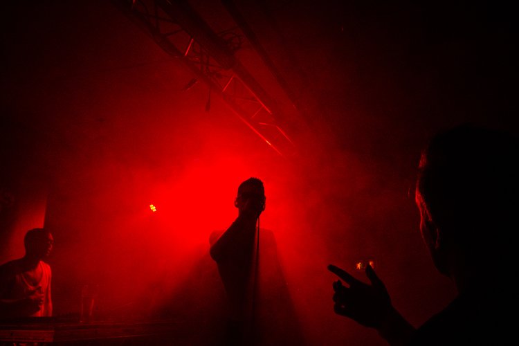 Silhouetten von Menschen auf einer rot beleuchteten Bühne.
