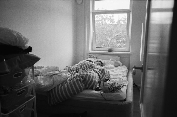 Eine Person schläft in einem Schlafzimmer. Durch das offene Fenster sind Bäume zu sehen.