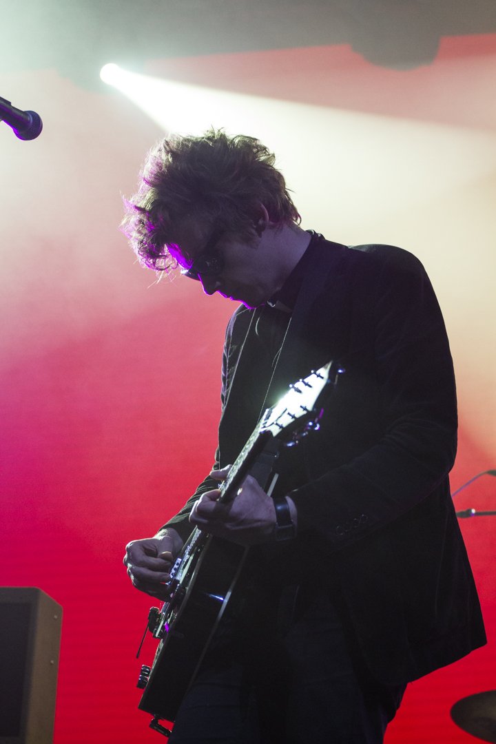 Die Silhouette eines Musikers mit Akustikgitarre vor farbigen Bühnenscheinwerfern.