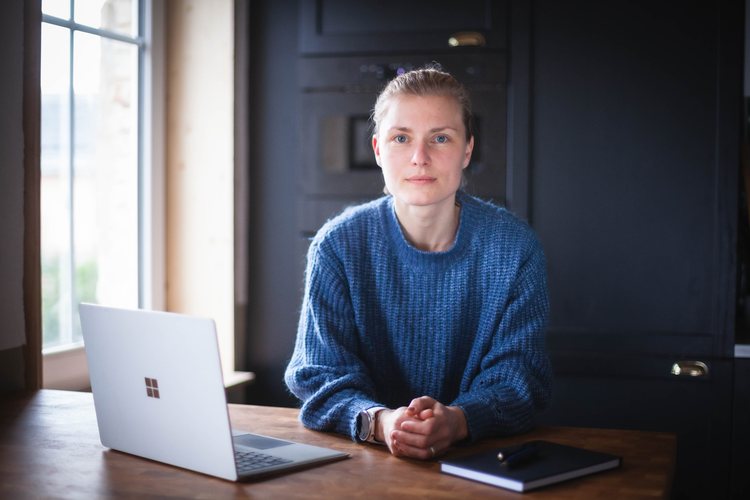 Ein Porträt am Holztisch mit Laptop und Notizbuch.