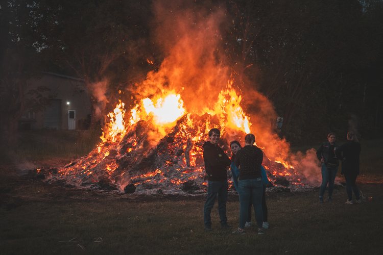 People gathered beside a large bonfire at dusk.