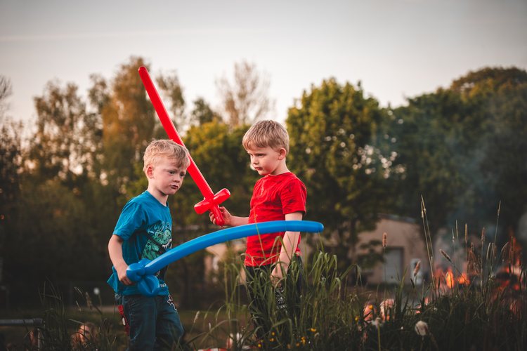 Children playing with balloon swords outdoors.