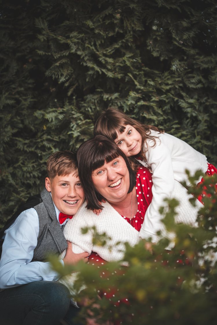 A woman and two children smiling together behind white flowers.