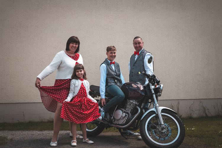 Eine Familie posiert spielerisch neben einem Motorrad.