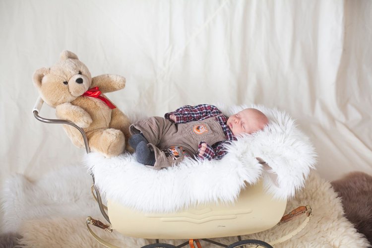 Ein schlafendes Baby in einem alten Kinderwagen neben einem Teddybären.