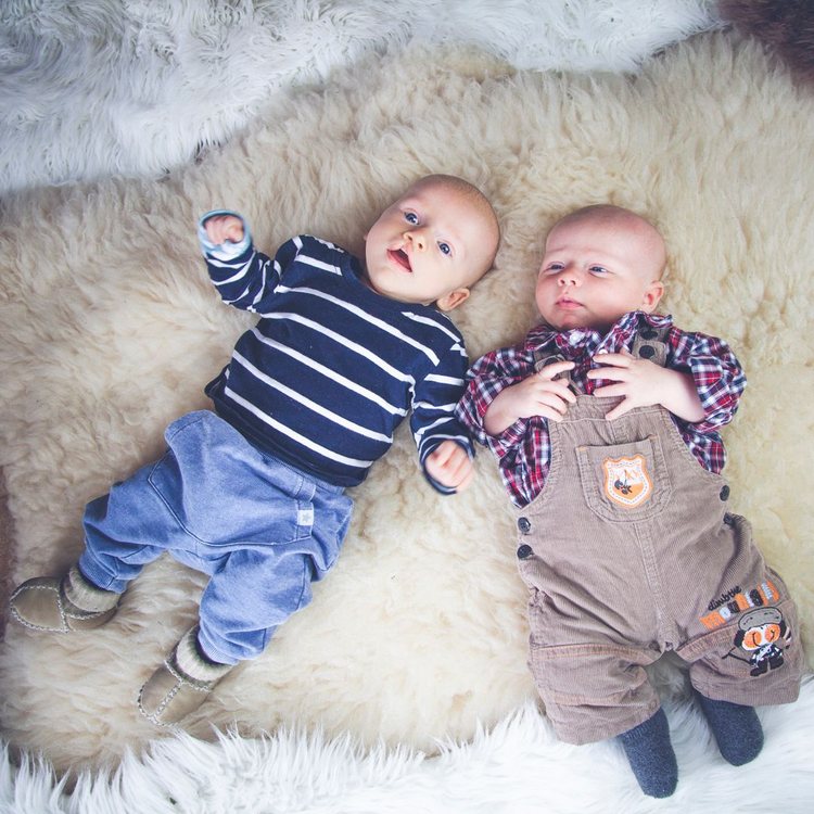 Zwei Babys liegen nebeneinander auf einer weichen Decke.