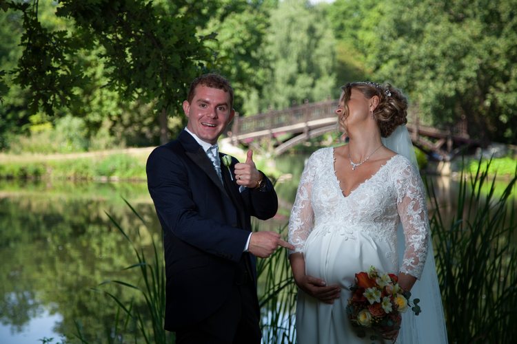 Das Hochzeitspaar lacht am Wasser.