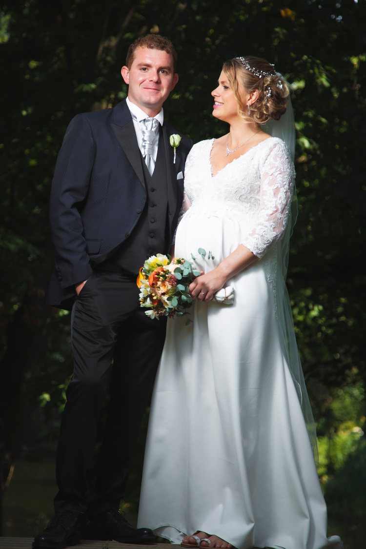 Ein Hochzeitsporträt in voller Länge vor grünem Laub.
