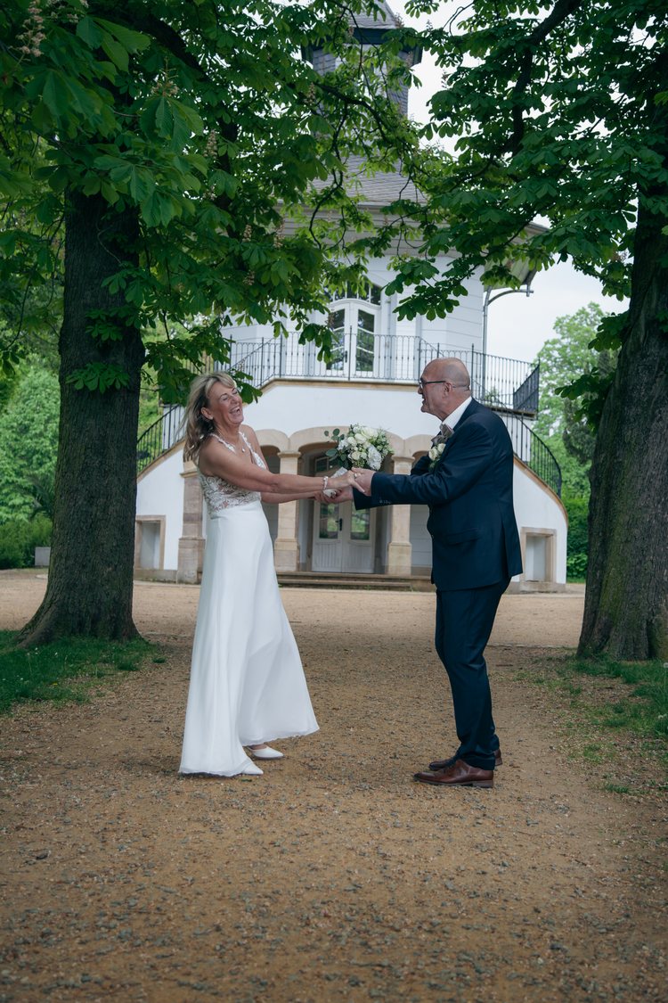 Das Hochzeitspaar lacht gemeinsam unter den Bäumen.
